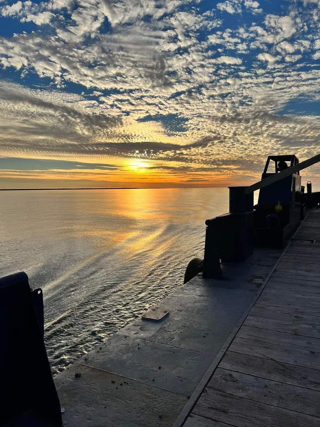 Work vessel silhouetted against a bright sunset over the sea
