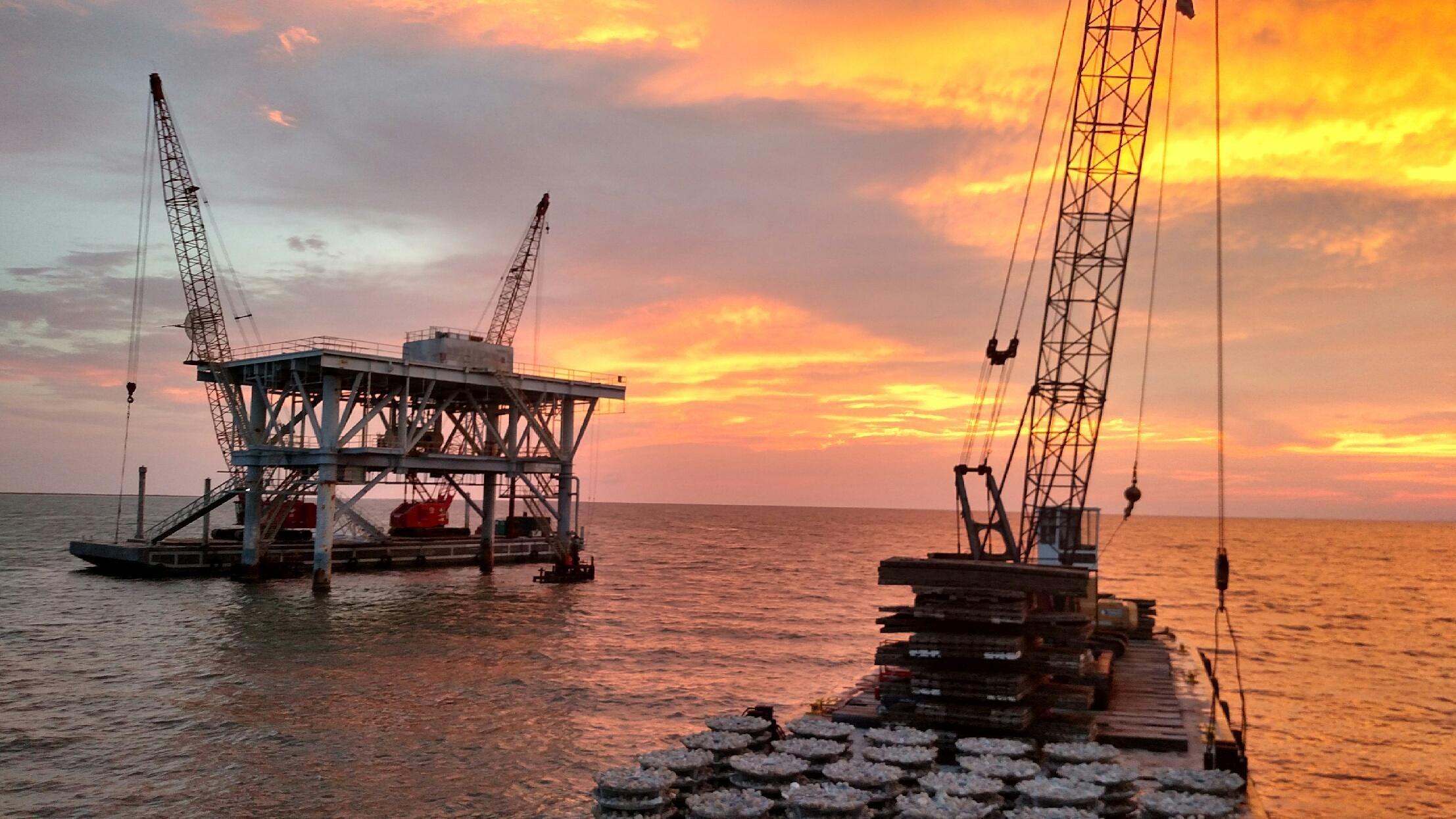 Silhouetted offshore reef structures and crane barges at sunset