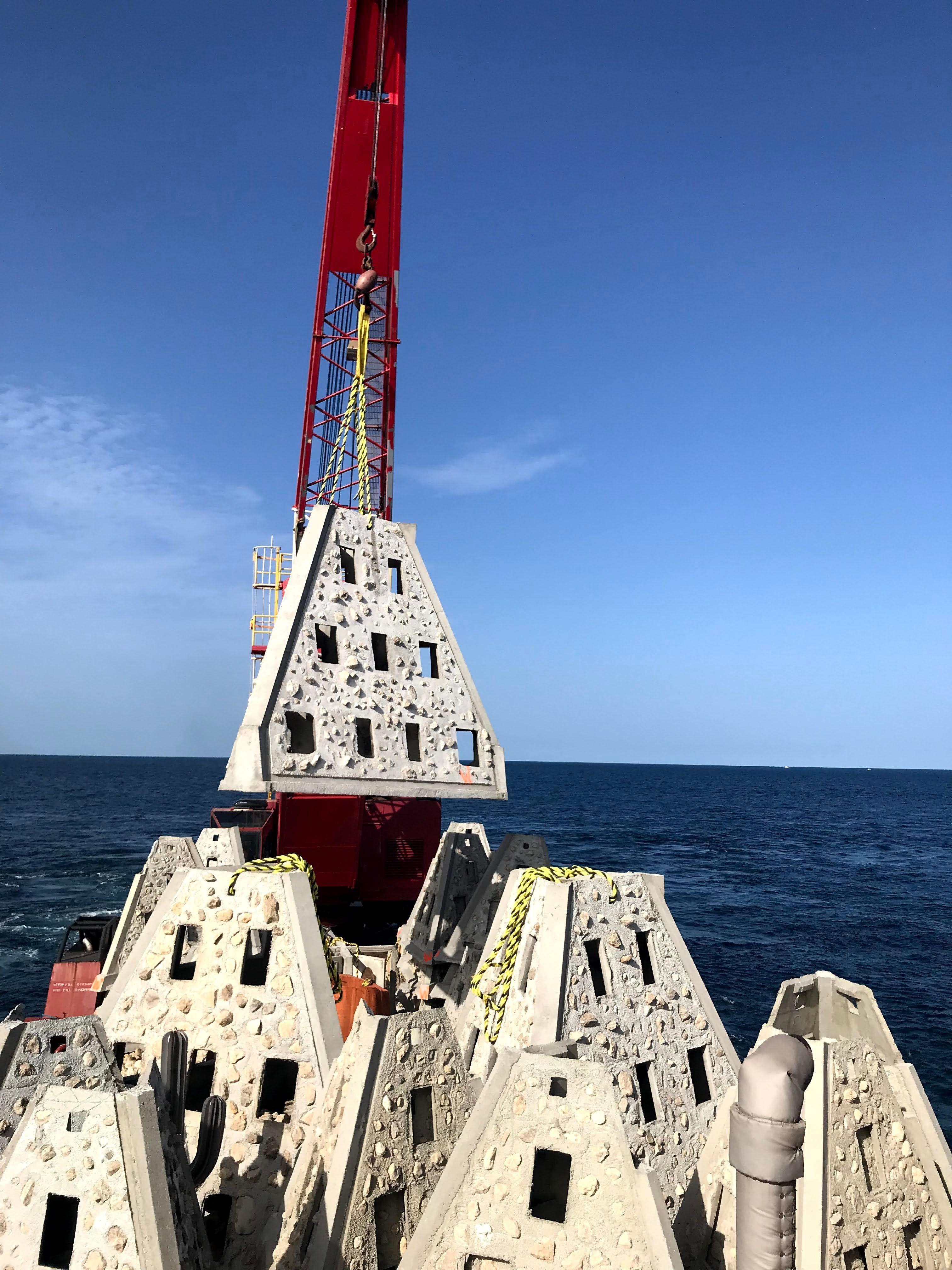 Concrete reef modules stacked on a barge beneath a crane boom