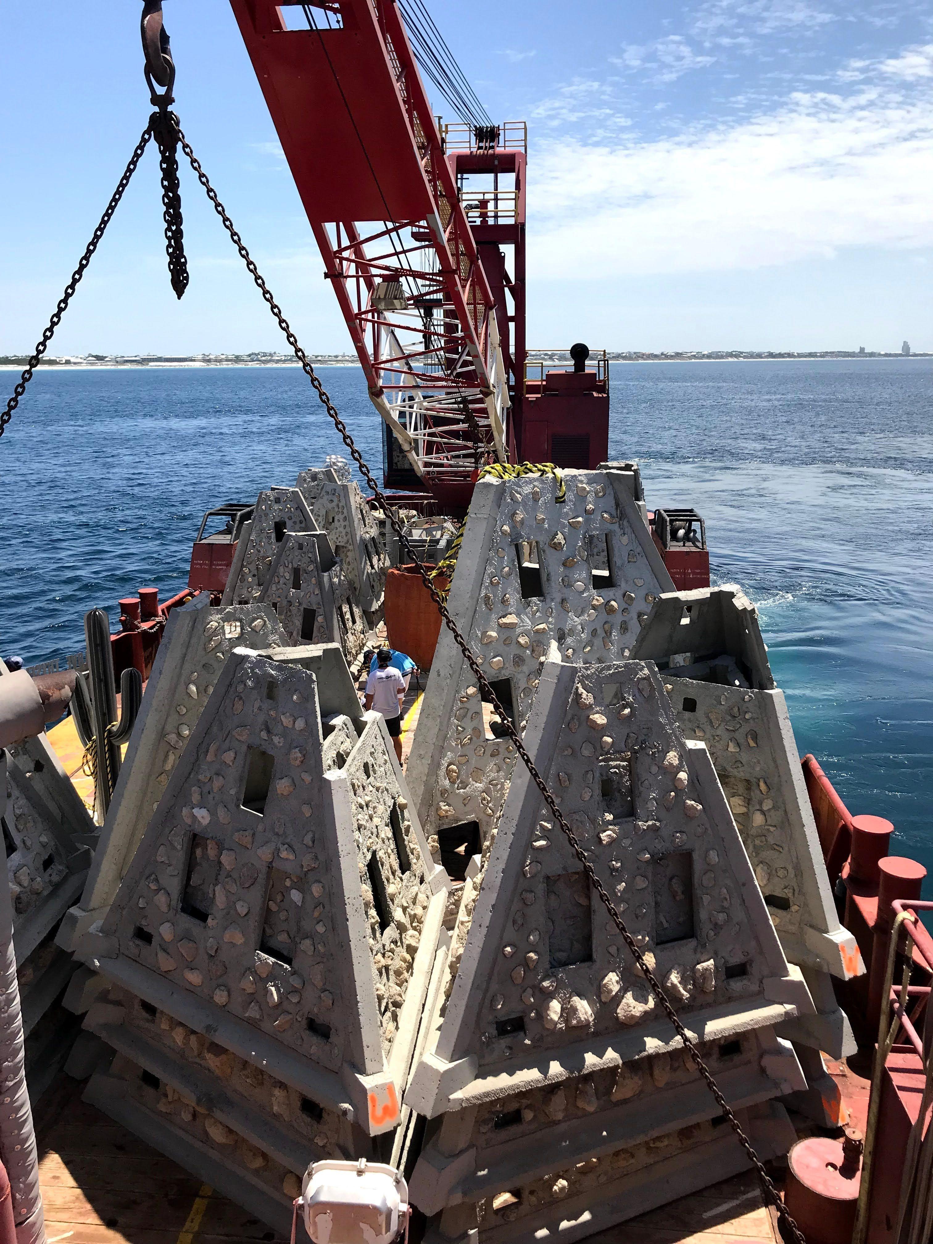 Stacked concrete reef modules lifted beside a marine construction vessel