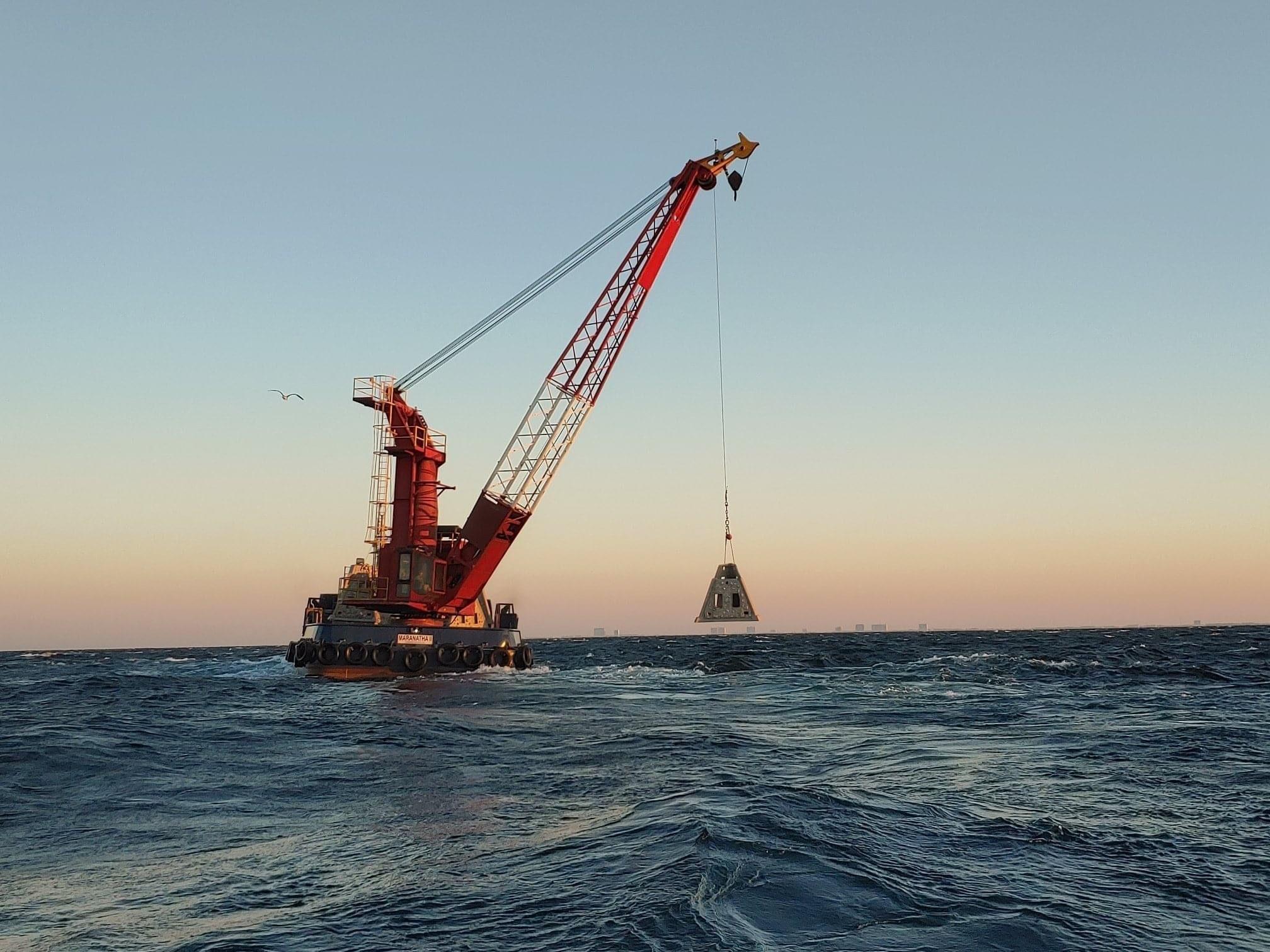 Crane barge lowering an artificial reef structure into the sea at sunset