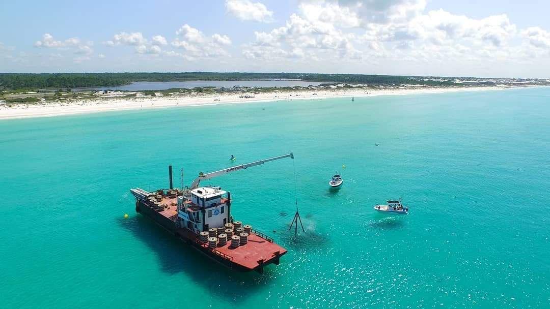 Work vessel and crane rigging over turquoise water during reef deployment