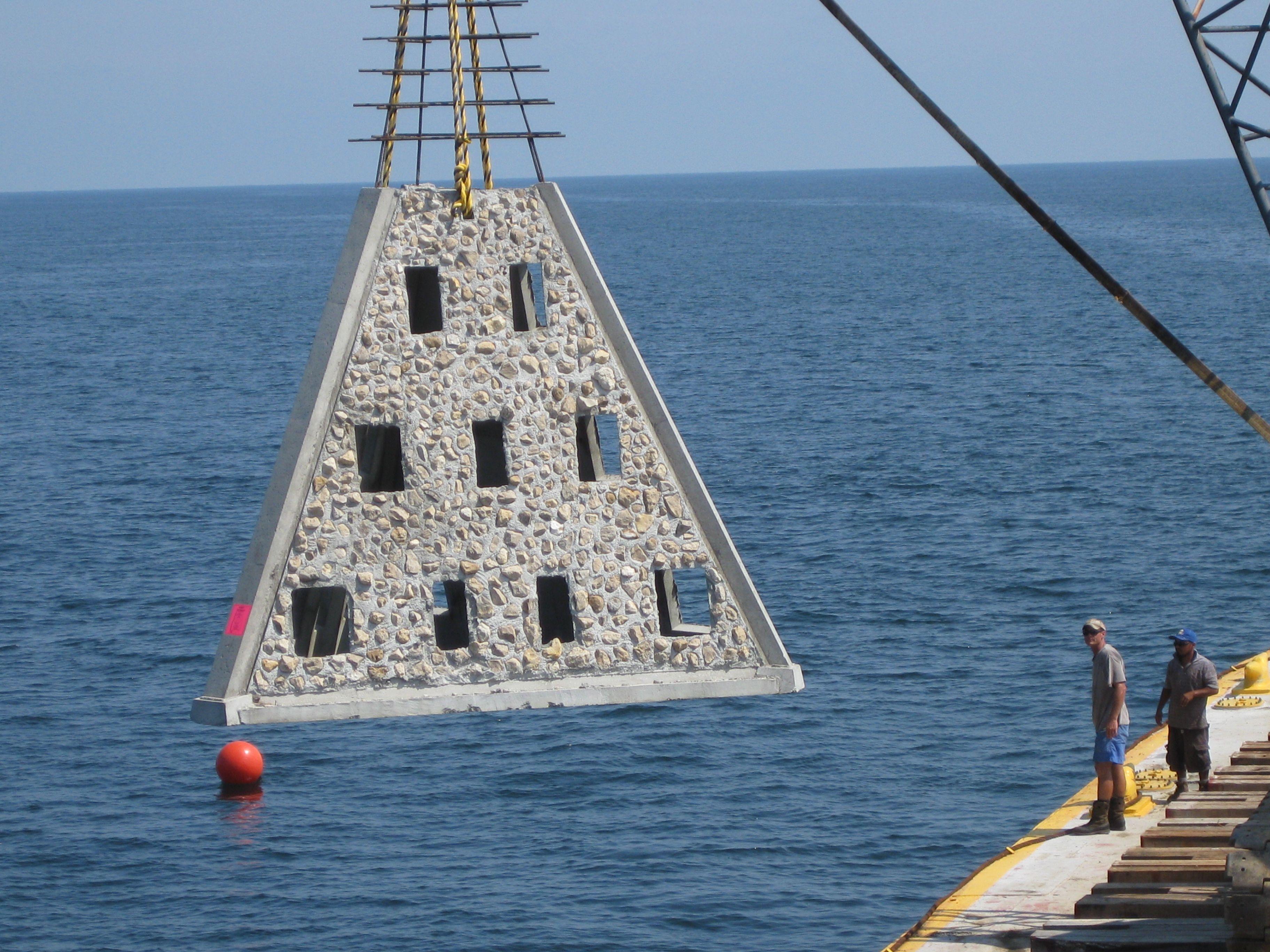 Pyramid-shaped concrete reef module suspended beside a work vessel