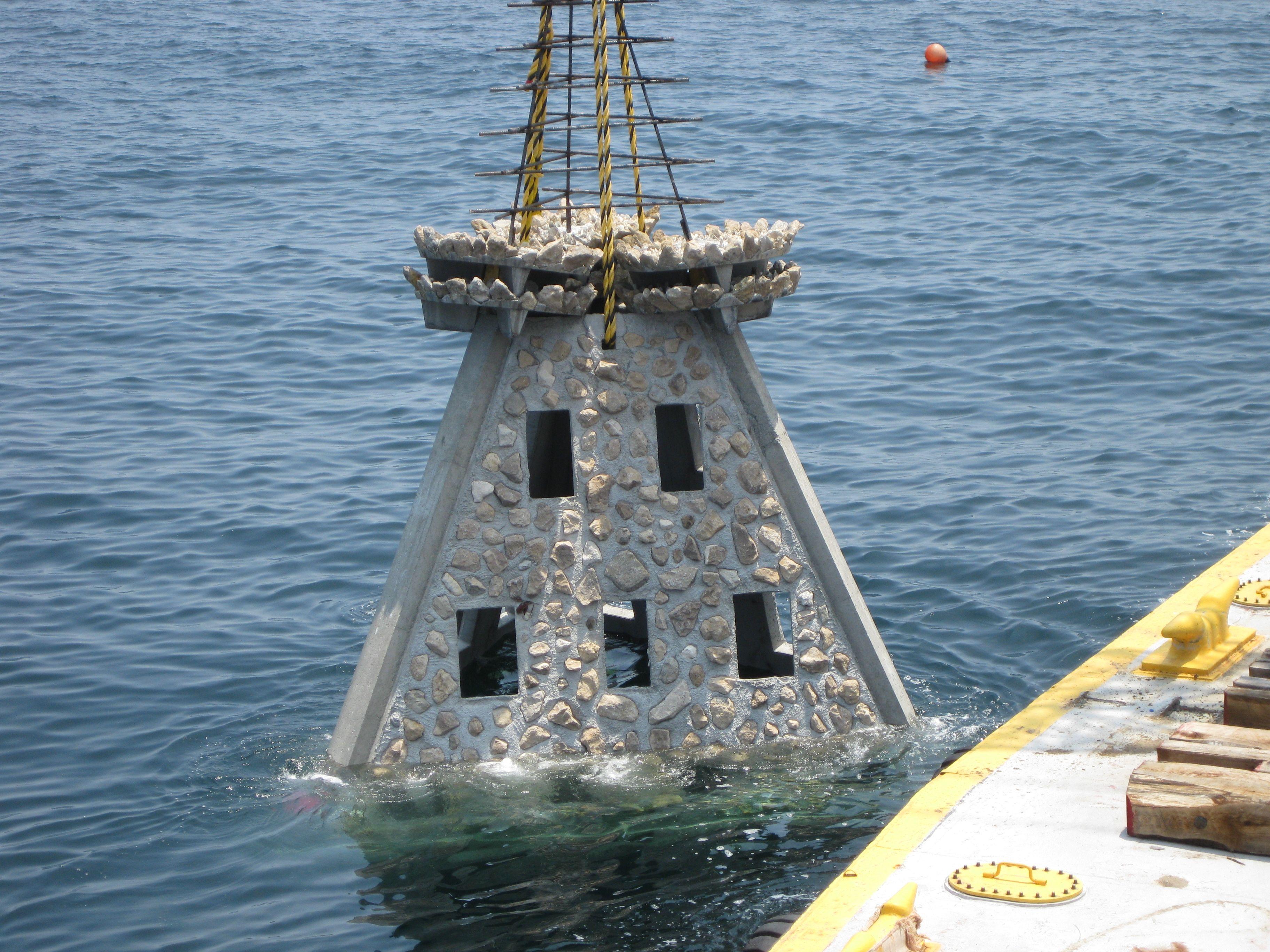 Pyramid-shaped reef module suspended alongside a work vessel