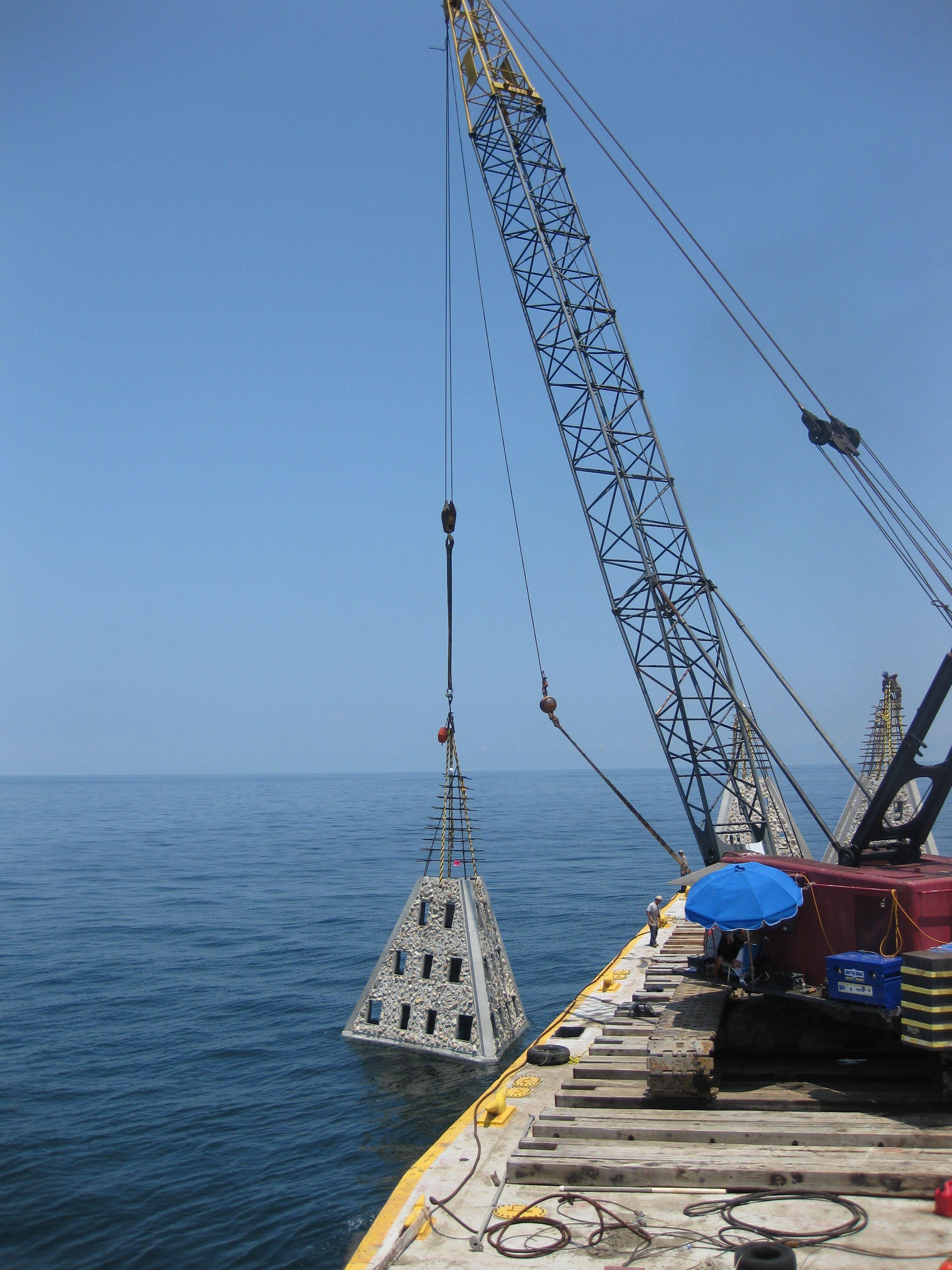 Crane lifting an artificial reef module from a marine construction barge