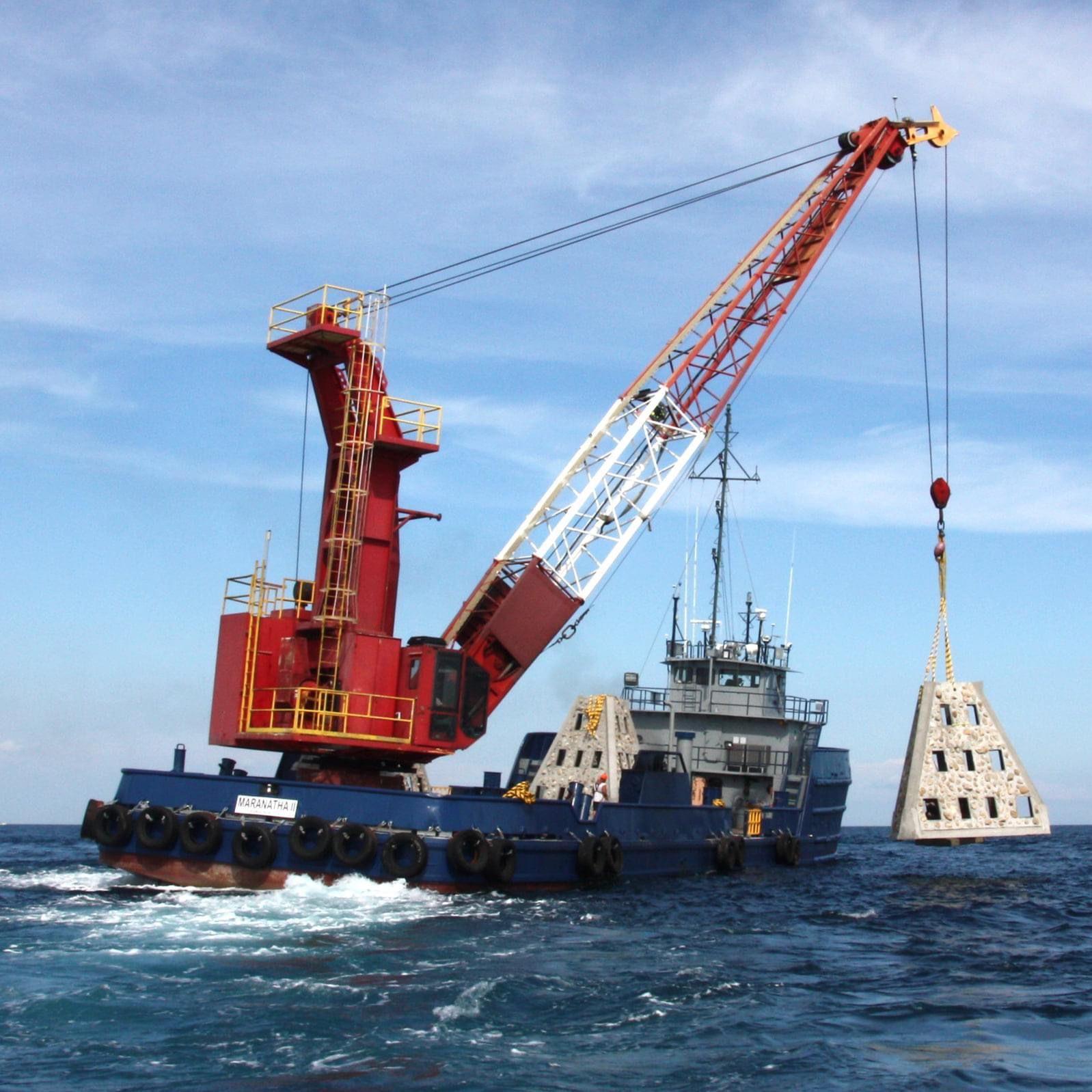 Crane barge lifting a pyramid artificial reef module offshore