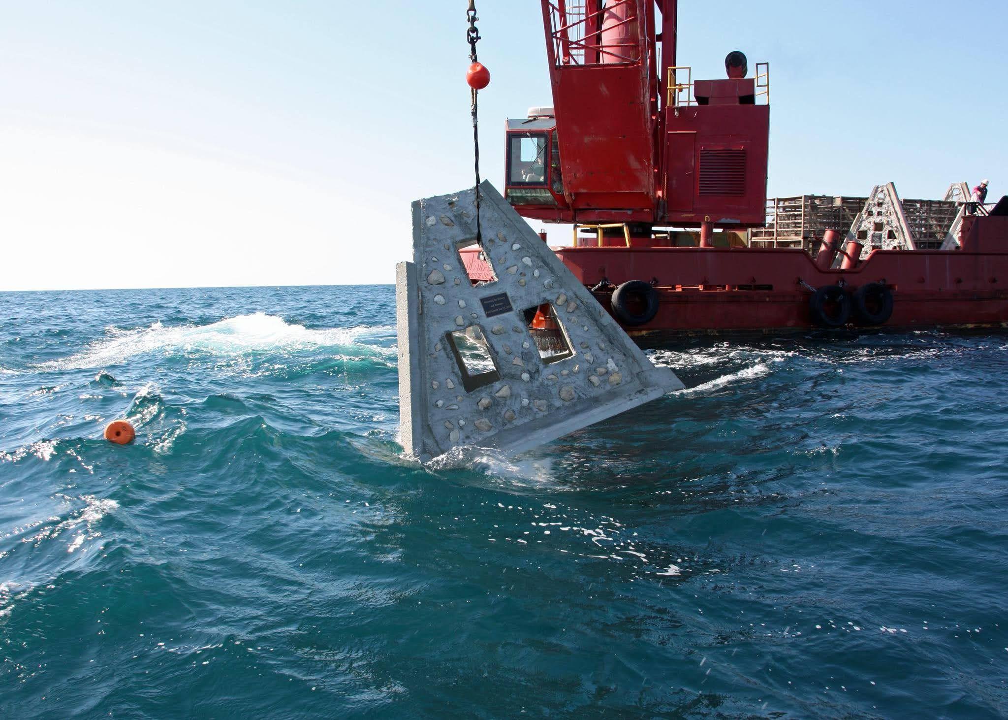 Pyramid artificial reef module entering the water beside a crane barge