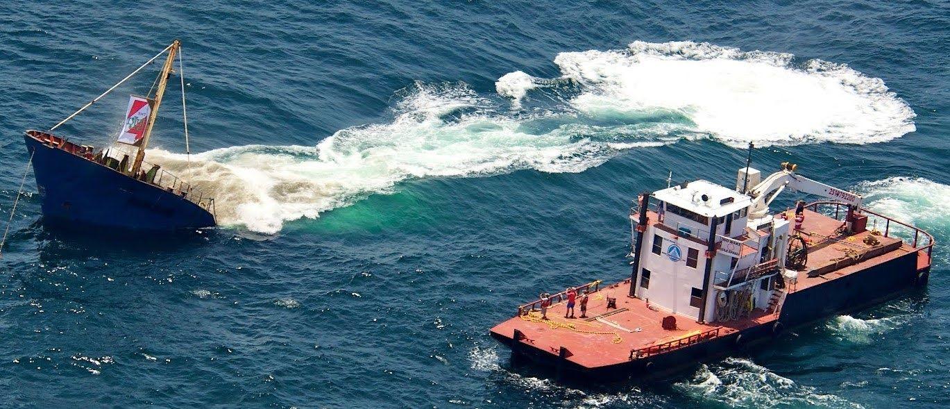Vessel nearly submerged with a tugboat alongside during a controlled sinking