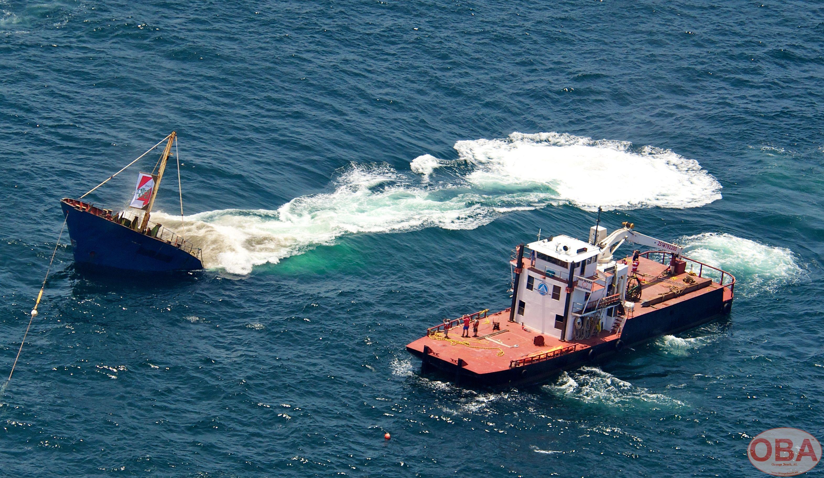 LuLu vessel disappearing beneath the water beside a support tugboat